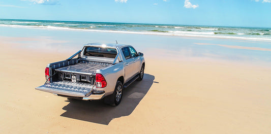 Silver ute with DECKED drawer system parked on open beach during Easter